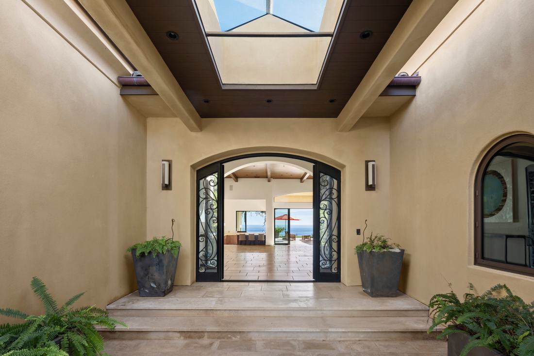 The entry court: iron-and-glass doors with the ocean visible straight through the house